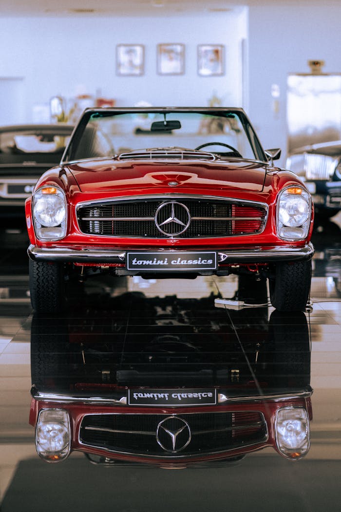 Classic red Mercedes Benz convertible on display in a showroom, perfectly reflected on the polished floor.
